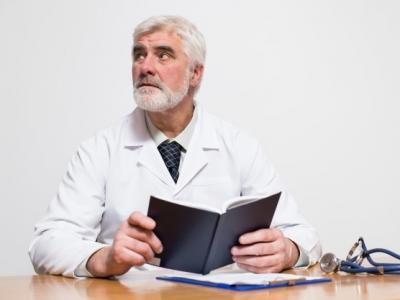 Imagem mostra médico em cima da mesa com livro aberto