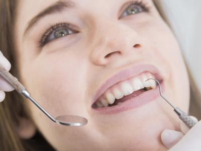Imagem mostra mulher tendo dentes examinados em dentista