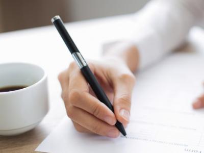 Imagem mostra mão de uma pessoa com caneta na mão escrevendo em papel